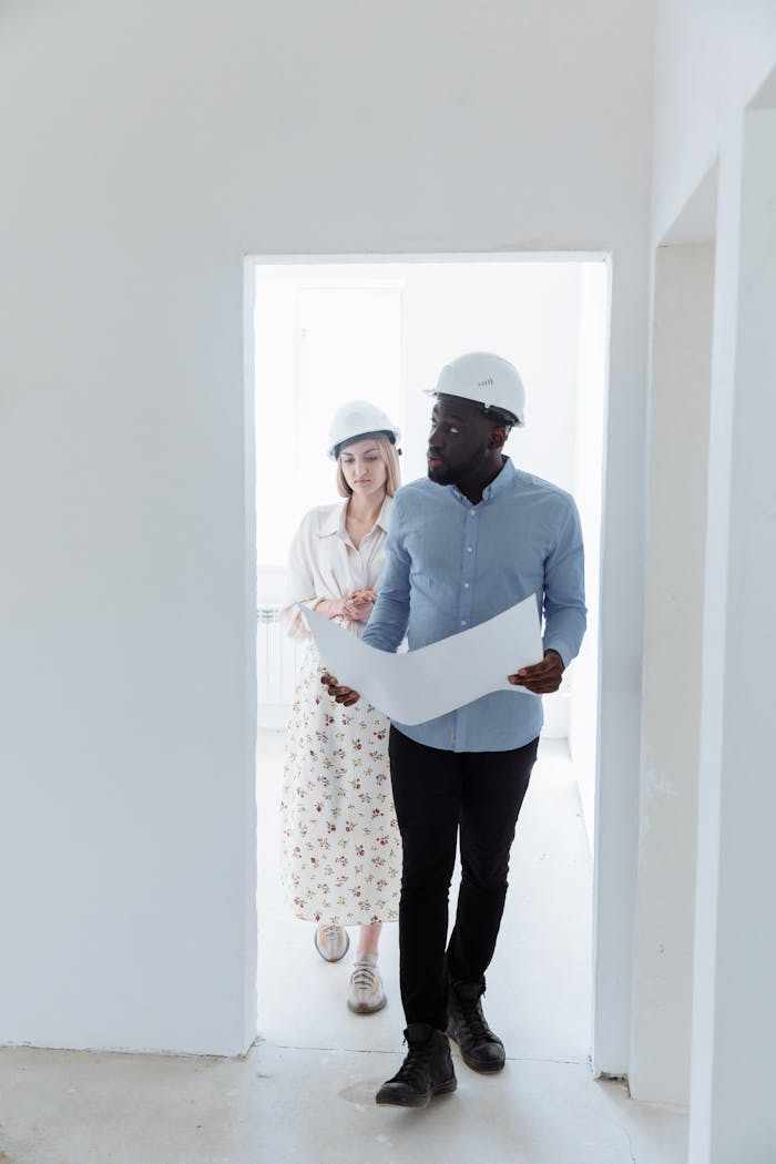 Two architects in hard hats reviewing blueprints inside a modern building.