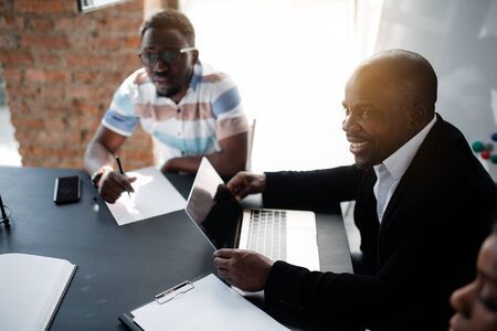 149632451 portrait of a black director in a black suit sitting at a laptop next to him are his african